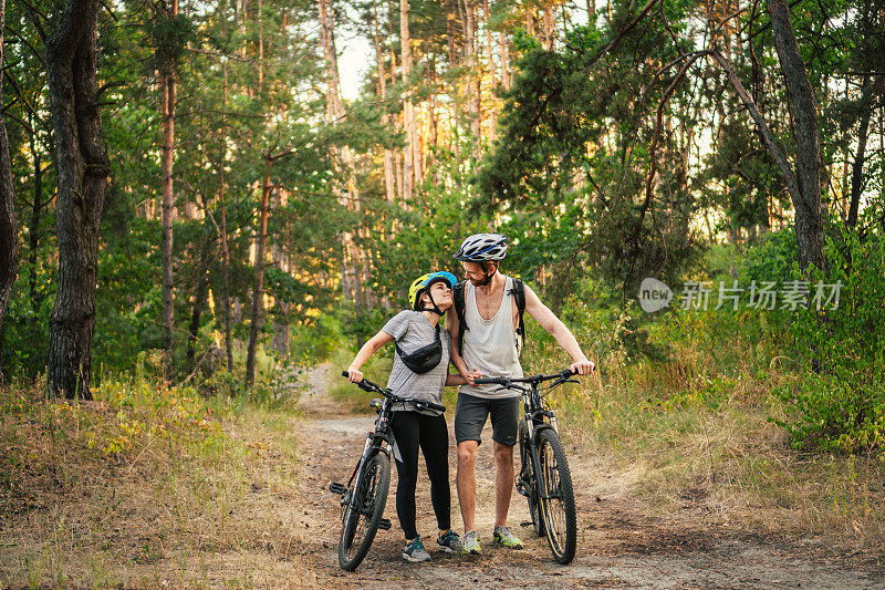 Gorgeous couple riding on bikes in park forest. Romantic trip by bicycles. Active weekend. Sport couple. Man and woman cyclists. Eco friendly transportation. Сouple with mountain bikes on the path